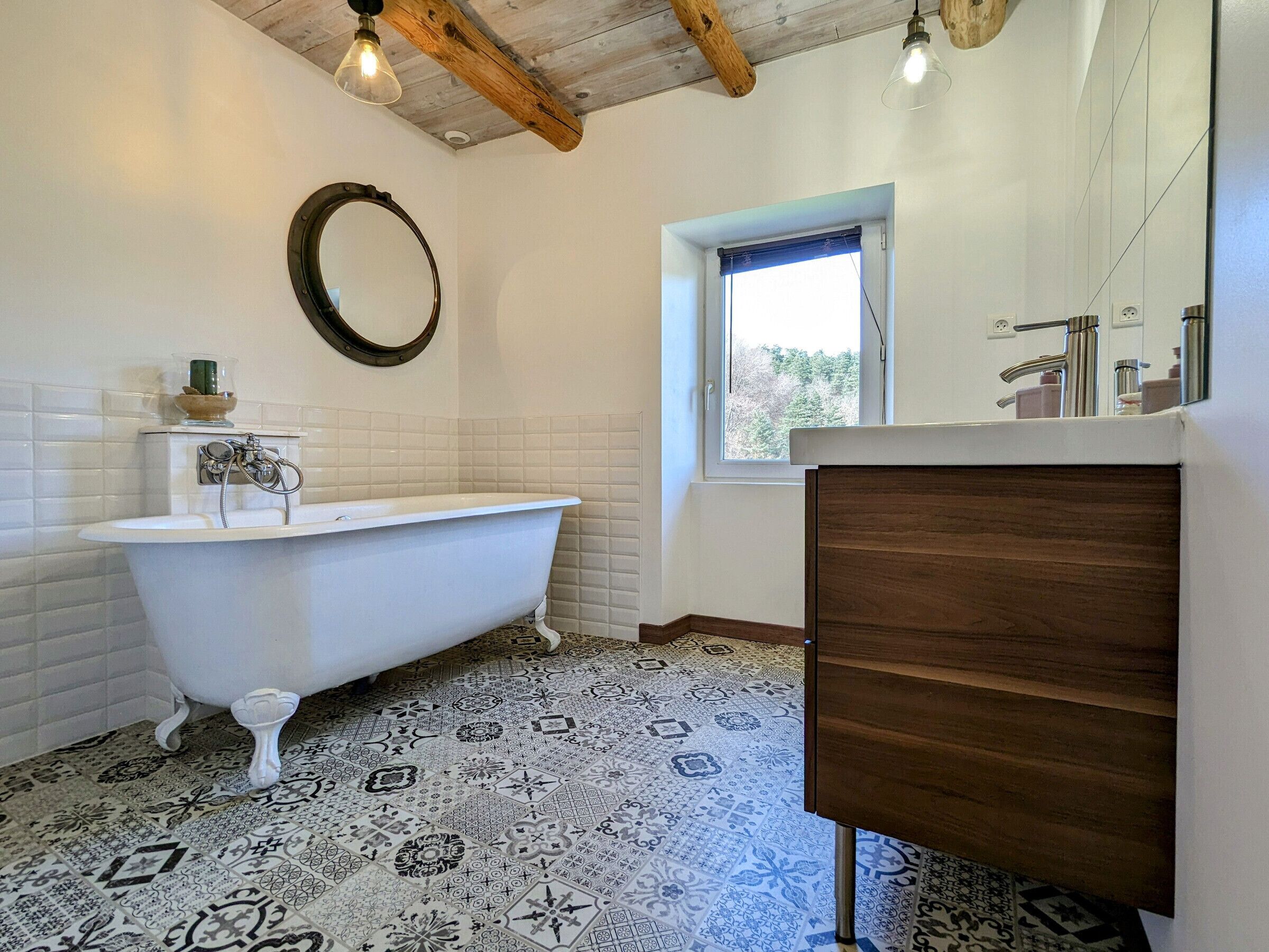 A bathroom with a freestanding bathtub, a wooden vanity, a mirror, and patterned floor tiles.