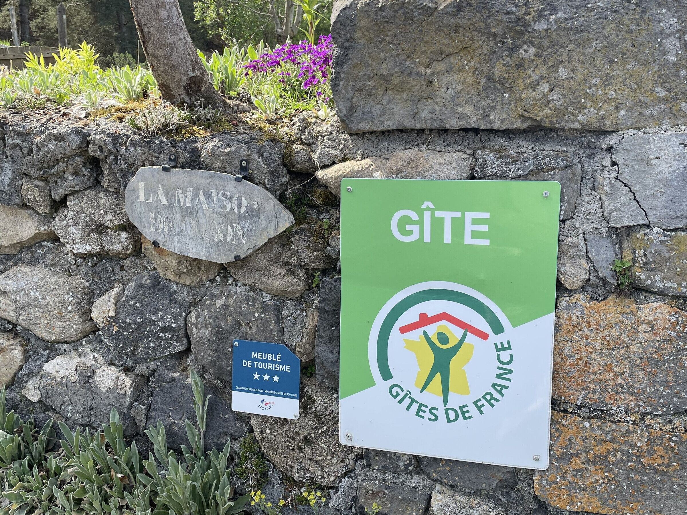 Una pared de piedra con un cartel que indica 'GÎTE GÎTES DE FRANCE' y un cartel más pequeño debajo con la inscripción 'MEUBLÉ DE TOURISME'.