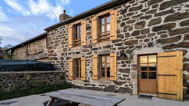 Un edificio de piedra con contraventanas de madera, una puerta de madera y una mesa de picnic al frente.