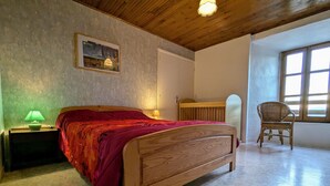 Un dormitorio con una cama de madera, una mesita de noche con lámpara, una silla de mimbre y una ventana con luz natural.