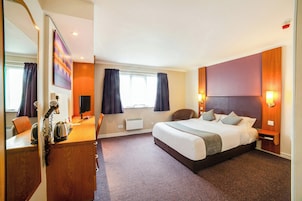 Habitación de hotel con una cama, un escritorio con una tetera, una silla, un espejo y una ventana con cortinas.