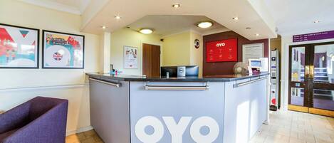 A reception area with a counter labeled 'OYO,' a seating area with a purple chair, and a wall with framed pictures.
