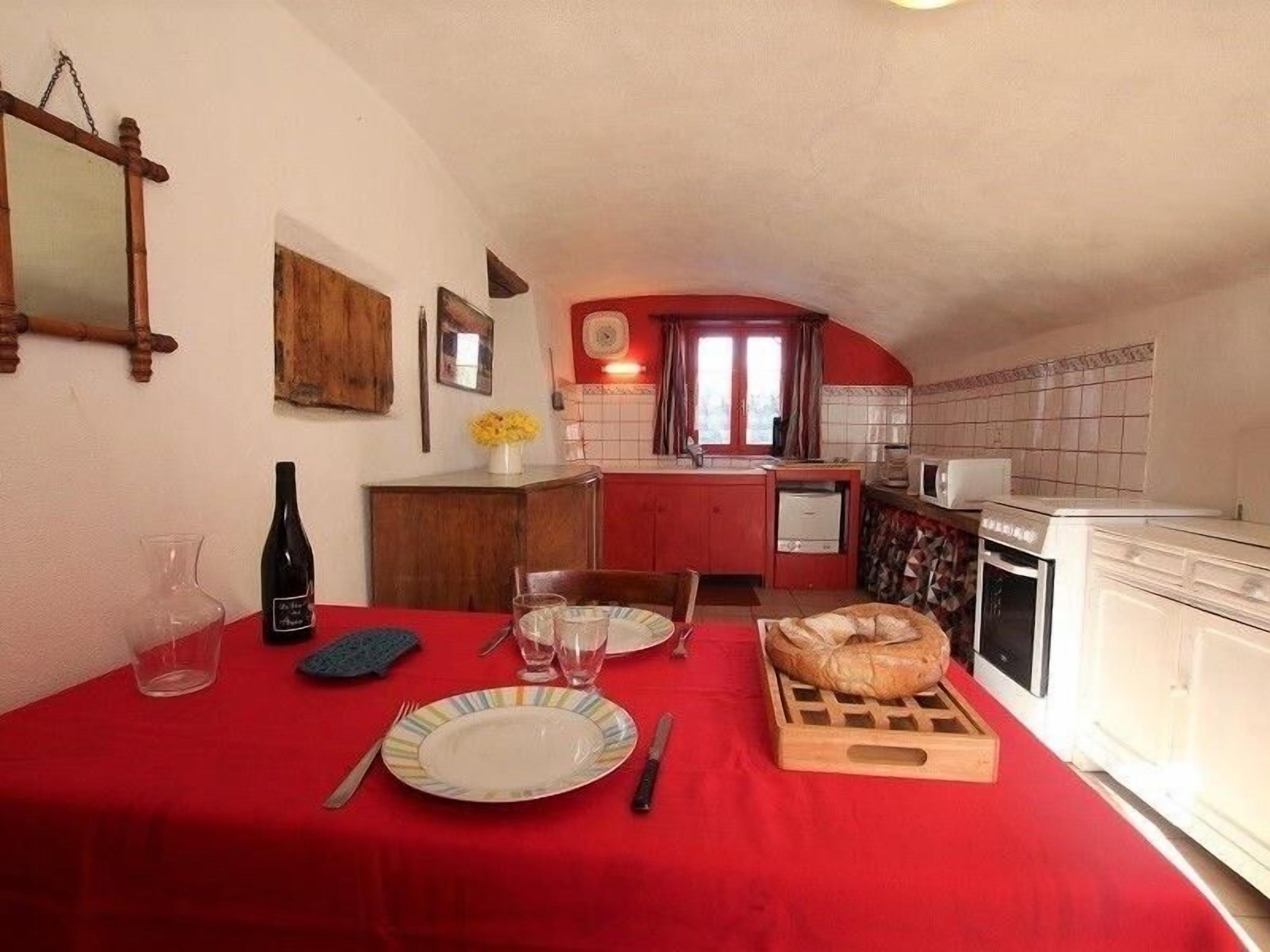 Un comedor con mantel rojo, una hogaza de pan y una botella de vino.