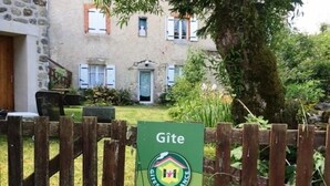 Skilt for Gîte de France på et træværk hegn foran en bygning i sten med en have.