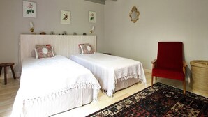 A bedroom with two beds, a red chair, a woven basket, and a patterned rug.