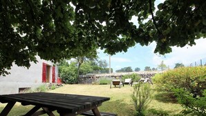A picnic table in a grassy outdoor area with a stone wall and a red building in the background.