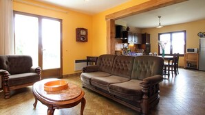 A living room with a sofa, armchairs, and a coffee table. There is a kitchen in the background with cabinets and a microwave.