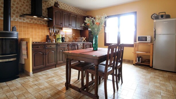 A kitchen with a dining table, chairs, a stove, cabinets, and a refrigerator.