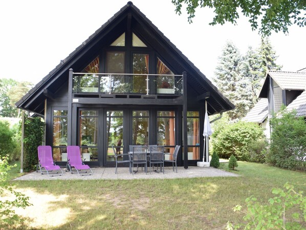 A two-story house with a balcony, large windows, and outdoor seating.