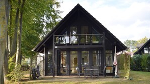 A two-story wooden building with large windows, a balcony, and a fenced outdoor area with chairs.