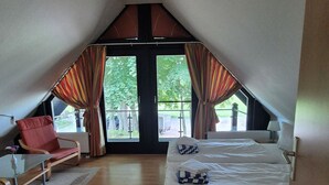 A bedroom with a bed, a chair, a table, and a view through a large window.