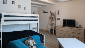 A bunk bed, a sofa, a TV, a bookshelf, and a small table in a room with wooden floors and white walls. - Apartment in the heart of Le Puy-en-Velay (Le Puy-en-Velay)