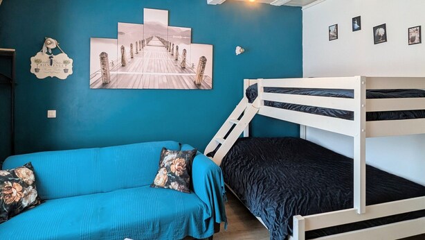 A room with a bunk bed, a sofa, a wall with a wooden pier painting, and a ceiling with exposed beams and hanging light bulbs. - Apartment in the heart of Le Puy-en-Velay (Le Puy-en-Velay)