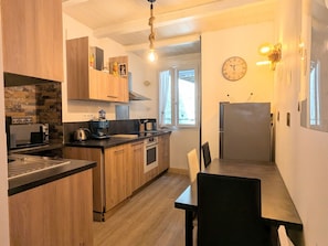 Une cuisine moderne avec des meubles en bois, un four encastré, une machine à café et un coin repas comprenant une table et des chaises.