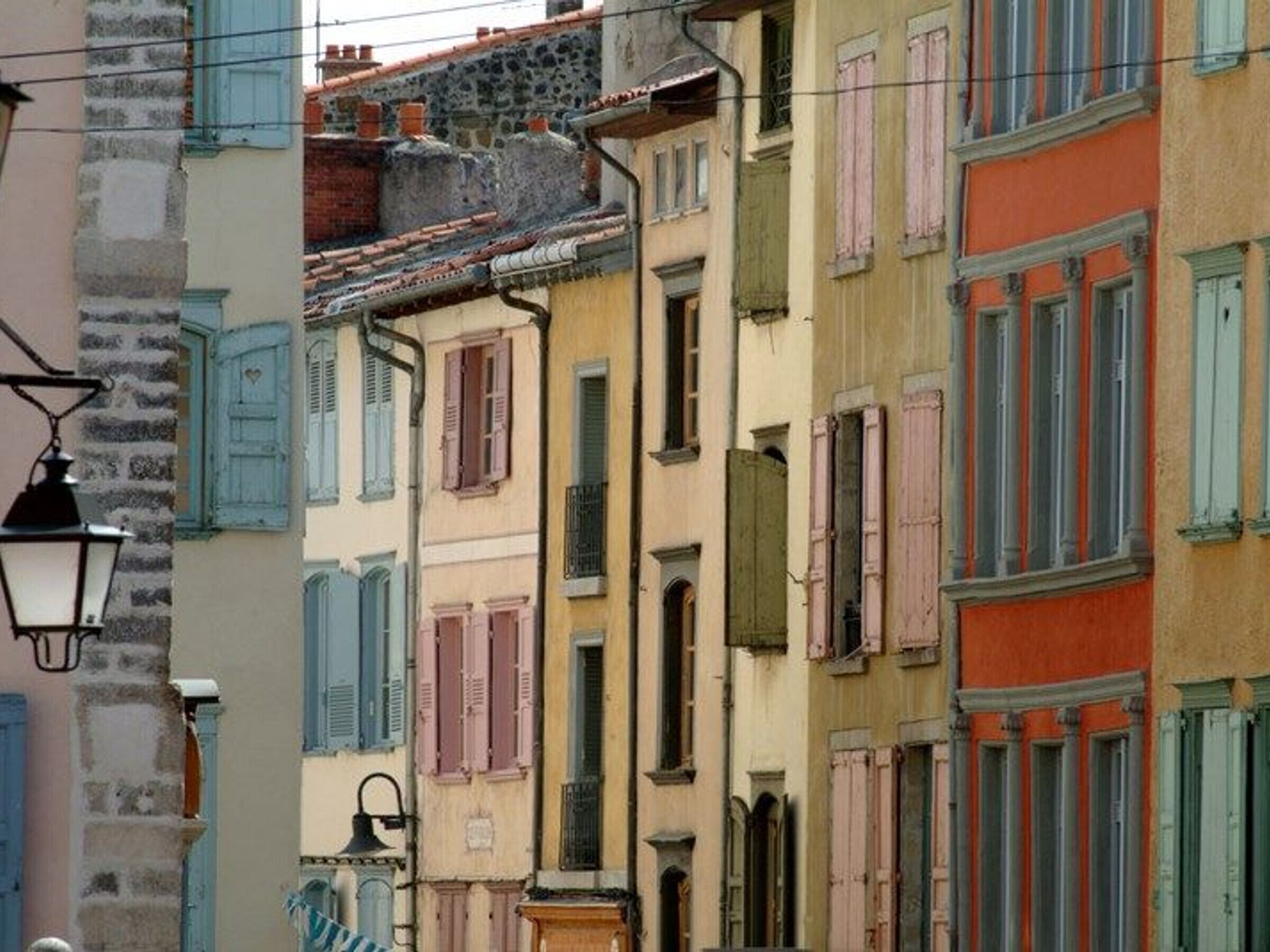 Une rangée de bâtiments colorés avec des volets, un lampadaire et un mur de pierre.