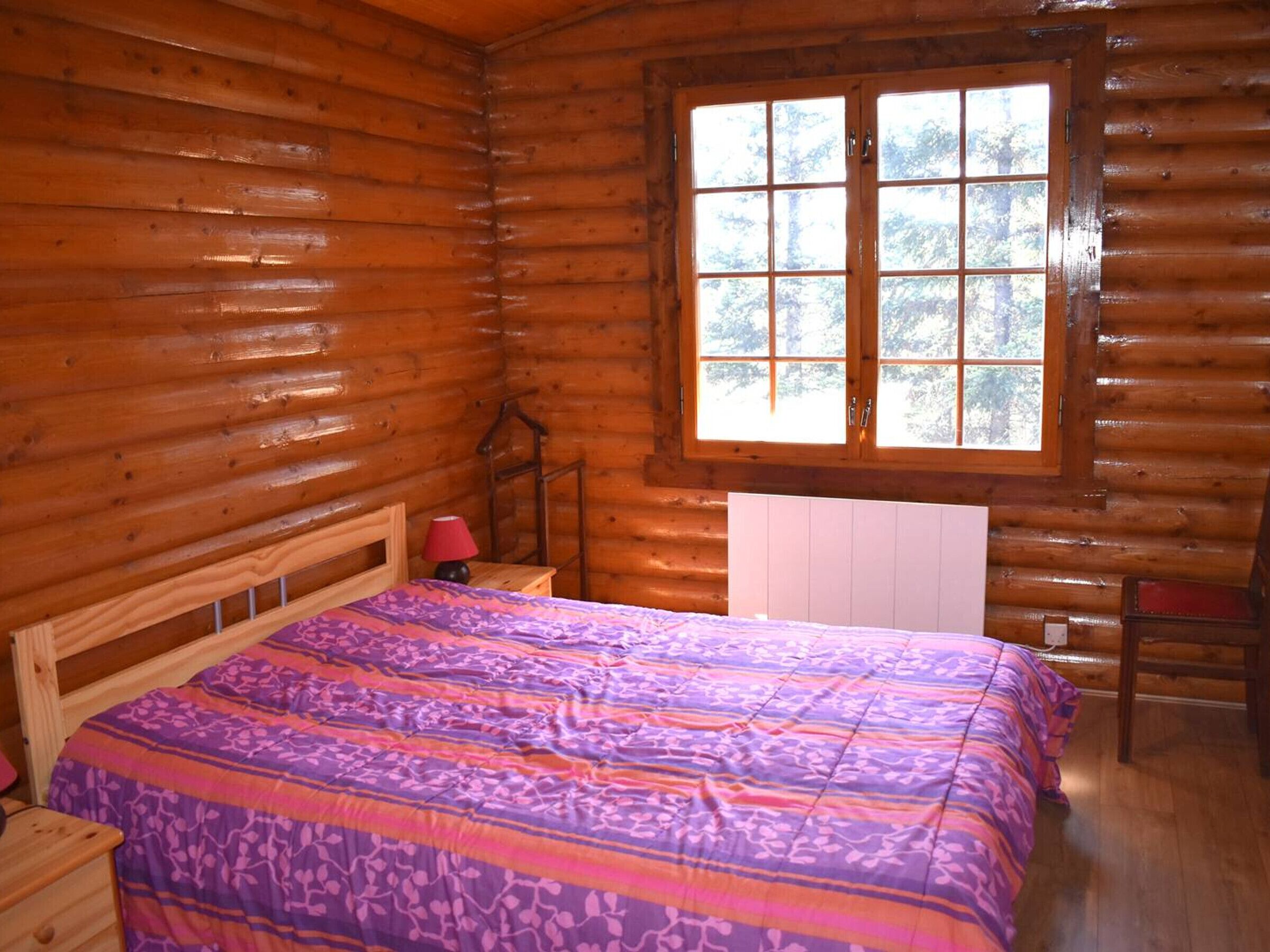 A wooden cabin room with a bed, a window, and a radiator.