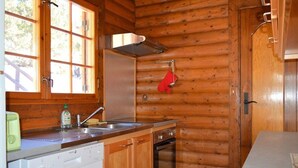 Une cuisine compacte aux murs en bois, dotée d’un four encastré, d’un lave-vaisselle et d’une fenêtre donnant sur les arbres.