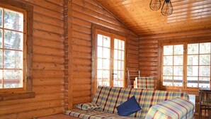 L’intérieur d’une cabane en rondins, avec un canapé à motifs écossais, une table basse en bois et de grandes fenêtres.