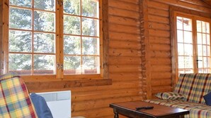 L’intérieur d’une cabane en rondins, avec des meubles à carreaux, de grandes fenêtres et une table en bois.