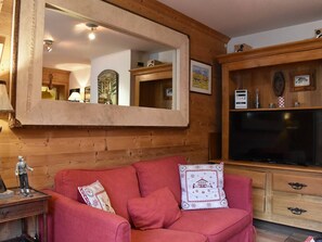 Een gezellige woonkamer met een grote spiegel, houten wanden, een rode bank en een flatscreen-televisie.