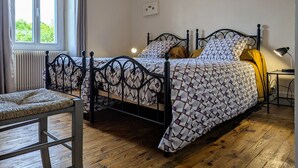 Une chambre à coucher comprenant un lit, une chaise, une table de chevet avec une lampe, une fenêtre et un interrupteur fixé au mur.