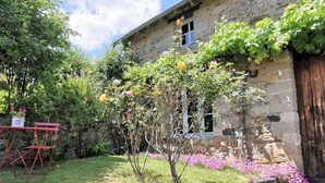 Un bâtiment rustique en pierre, doté d’un petit jardin où l’on trouve une variété de plantes et de fleurs.
