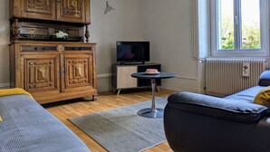 Un salon avec un meuble en bois, un téléviseur posé sur un meuble, un canapé et une fenêtre donnant sur un paysage verdoyant.