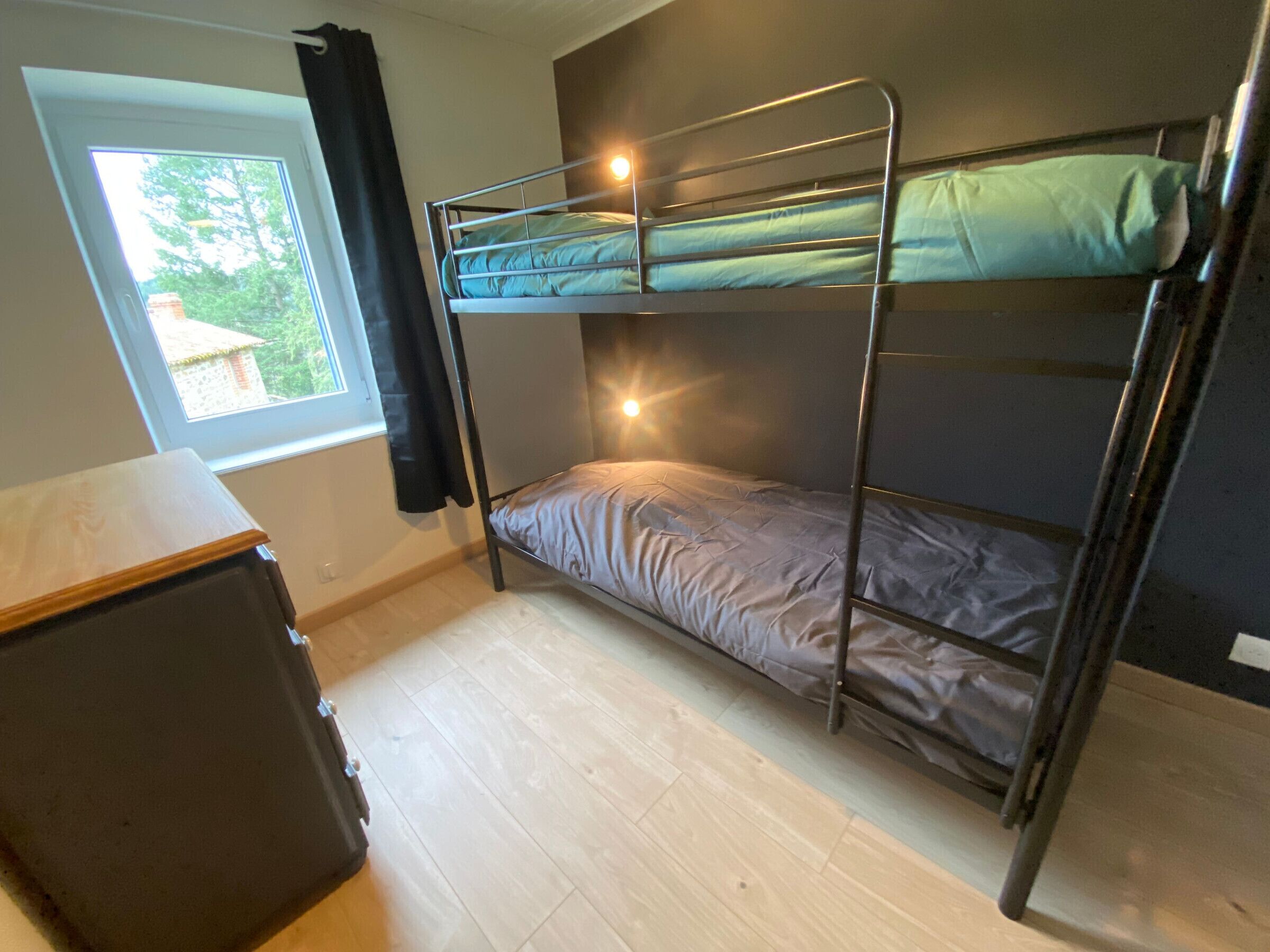Une chambre avec un lit superposé, une fenêtre, un bureau et un rideau.