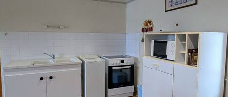A compact kitchen with a sink, a washing machine, an oven, and a microwave.