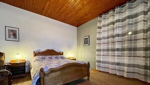 Une chambre à coucher avec un lit en bois, deux tables de chevet avec des lampes, une chaise et un rideau.