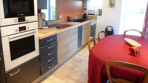 A compact kitchen with modern appliances, a dining area with a red table, and a view of the outdoors.