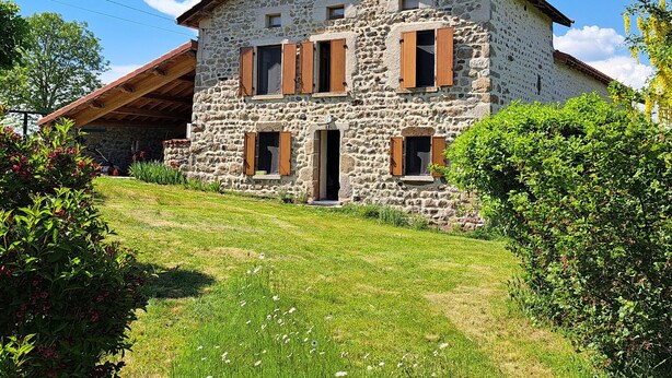 Ein Gebäude aus Stein mit einem geneigten Dach, hölzernen Fensterläden und einer Tür.