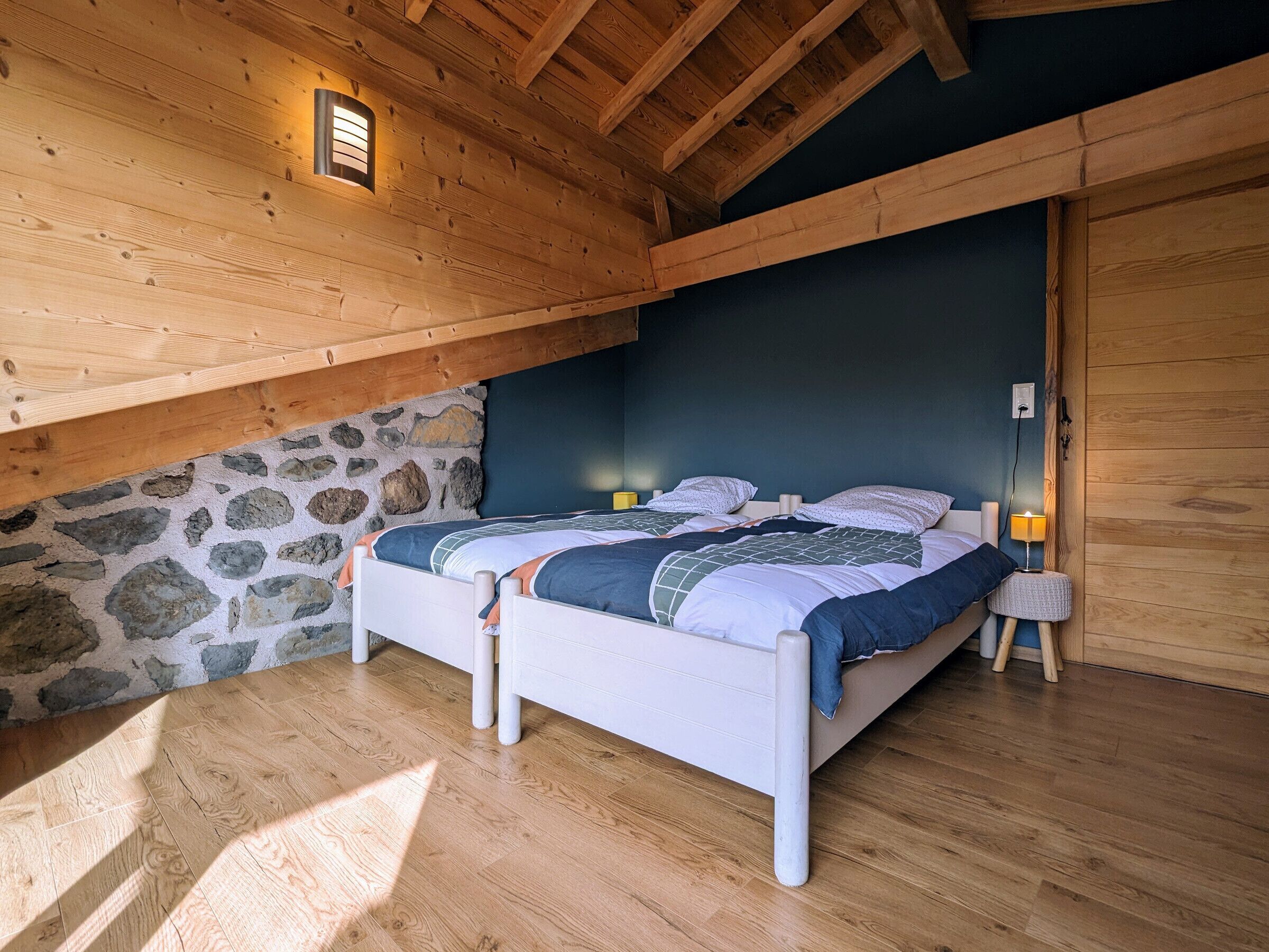 Ein Schlafzimmer mit Holzboden, Steinwand und einem Bett mit Patchworkdecke.