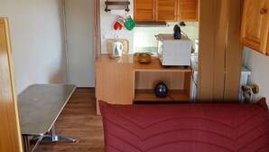 Kompakti keittiö, jossa on puiset kaapit, pieni työtaso ja vedenkeitin.