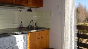Kompakti keittiö, jossa on puukaapit, pesukone ja ikkuna, jossa on pitsiverhot.