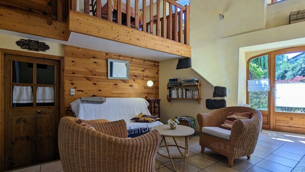 Una habitación acogedora con techo de madera, balcón, muebles de mimbre y una estantería.