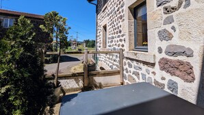 Un edificio de piedra con una reja de madera, una ventana con vistas y un área pavimentada en frente.