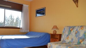 A bedroom with a bed, a chair, a nightstand, a lamp, and a window with a view of trees. - Cozy 2-Room Apartment for 6 with Terrace, Near Ski Slopes, Pet-Friendly (Bolquère-Pyrénées 2000)
