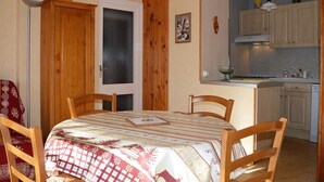 A compact kitchen with wooden cabinets and a small dining area with a table and chairs. - Cozy 2-Room Apartment for 6 with Terrace, Near Ski Slopes, Pet-Friendly (Bolquère-Pyrénées 2000)