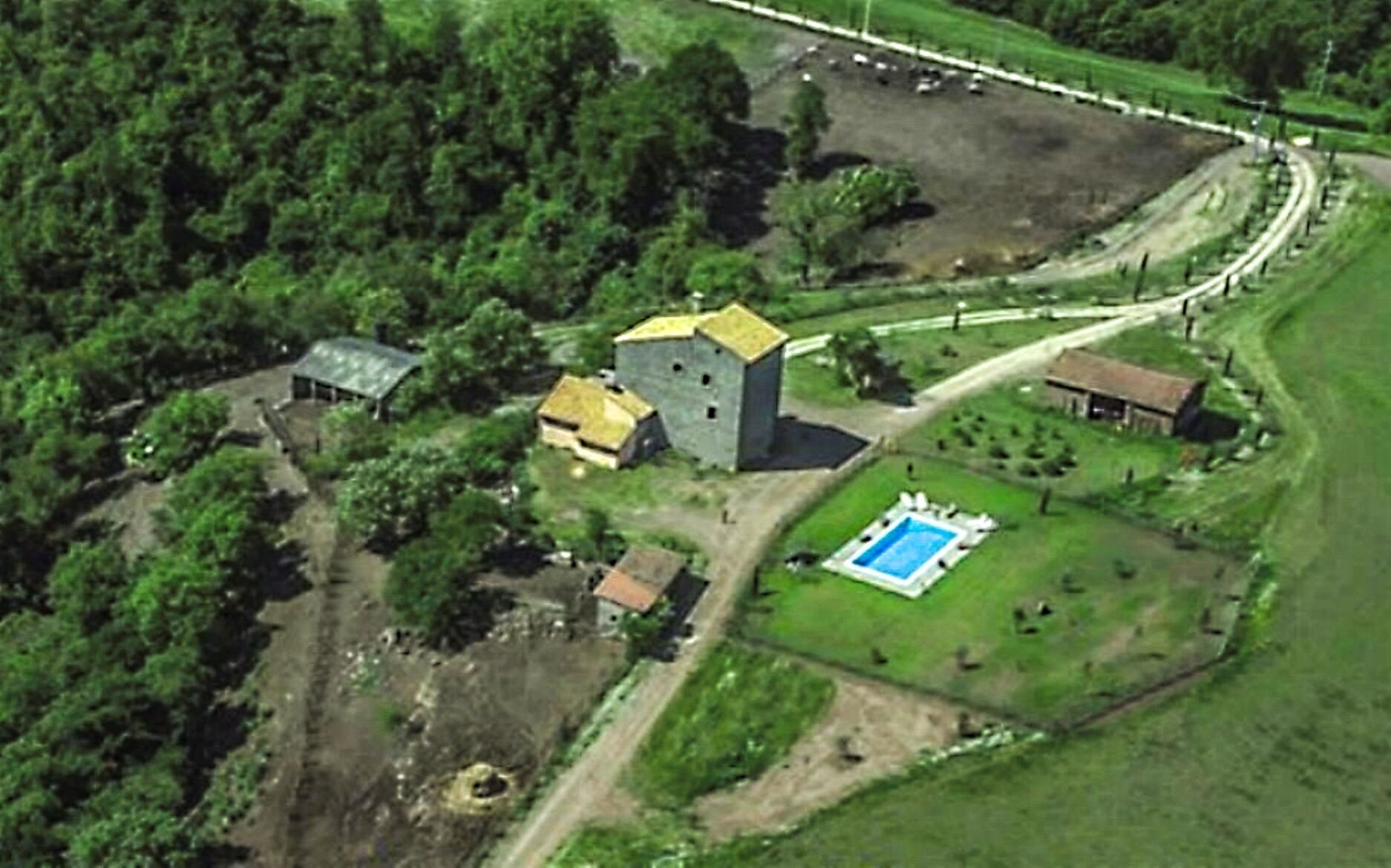 An aerial view of a rural property with a large stone building, a swimming pool, and surrounding greenery.