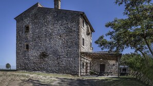 Un edificio de piedra con una chimenea, una estructura pequeña adosada con techo, y un árbol en primer plano.