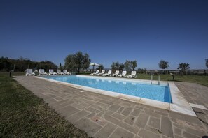 Una piscina rectangular con un borde de baldosas, rodeada de sillones blancos.