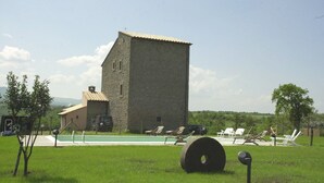 Un edificio de piedra con piscina y sillones de descanso en un área verde.