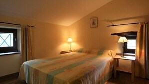 Ein Schlafzimmer mit einem Bett, zwei Nachttischlampen, einem Fenster mit Vorhängen und einem kleinen Tisch.