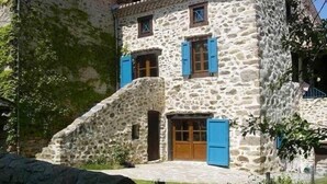Ein Gebäude aus Stein mit einer Treppe zum Eingang, Holztüren und blauen Fensterläden.