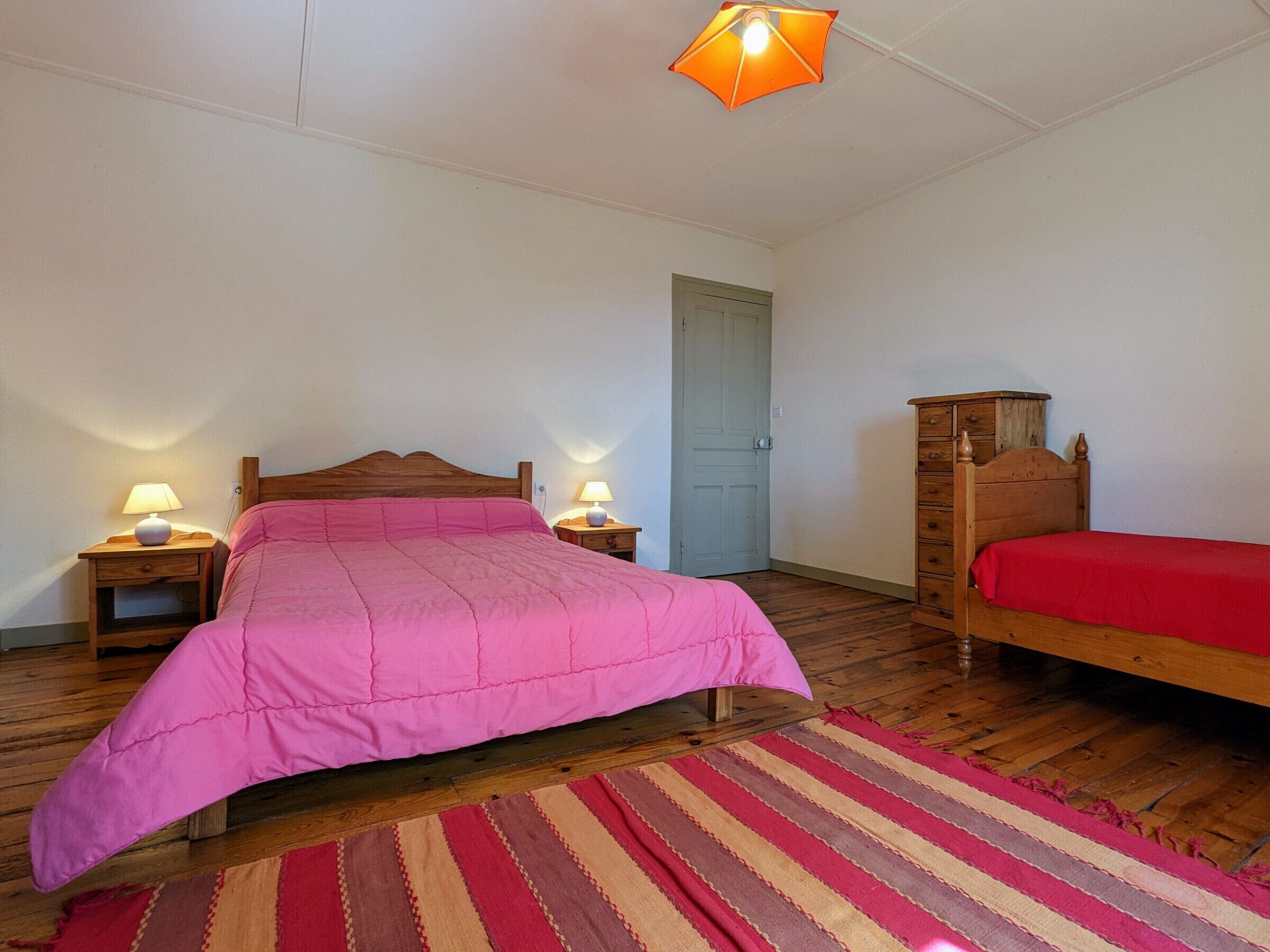 Une chambre à coucher avec un lit en bois, une commode en bois, un tapis à rayures et deux lampes de chevet.