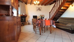 A cozy living room with a fireplace, wooden furniture, a dining table with chairs, and a staircase.
