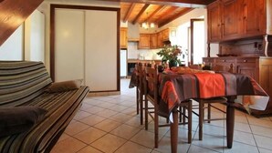 A dining area with a wooden table and chairs, a striped sofa, and a kitchen in the background.