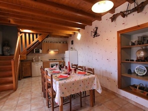 Une cuisine chaleureuse avec des meubles en bois, une table à manger pour quatre personnes et un escalier menant à l’étage supérieur.