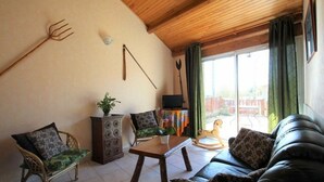 A cozy living room with a wooden ceiling, a sofa, two chairs, a coffee table, and a TV.